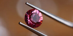 Jeweler In Workshop Holds Pink Stone In Tweezers